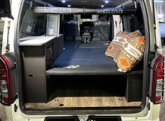 ハイエース後部の車中泊仕様。ダークグレーの収納キャビネットと折りたたみベッド、LED照明を備えた快適な室内