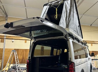 リアハッチを開けた白いハイエース。屋根にポップアップルーフテントを展開した状態。荷室の収納棚も見える