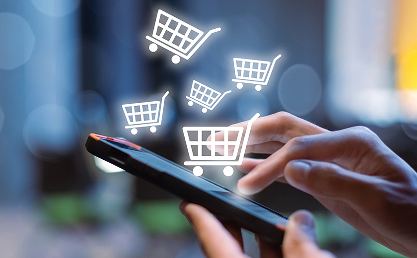 スマートフォンでオンラインショップを利用する様子。画面の上にショッピングカートのアイコンが浮かぶイメージ